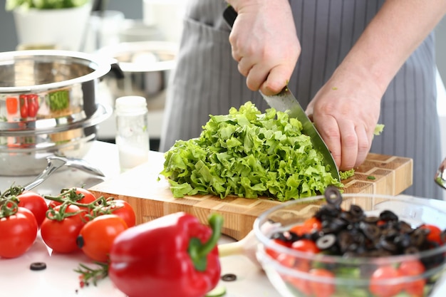 Il cuoco maschio prepara un'insalata di verdure e taglia le foglie di lattuga verde