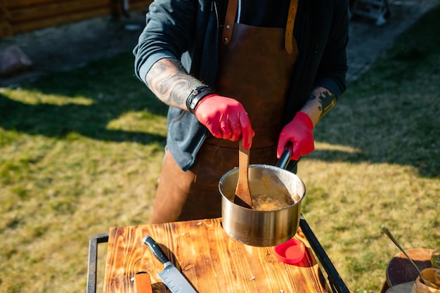 Il cuoco mescola il cibo in una casseruola Concetto della corretta cottura della carne Lo chef prepara delle patatine fritte una bistecca di manzo all'aperto