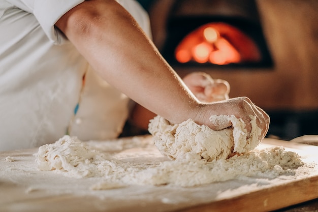 Il cuoco prepara l'impasto della pizza. Cucinando. Un uomo impasta con le mani l'impasto per fare la pizza in forno.