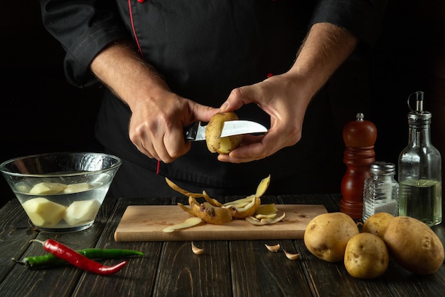 Il cuoco sbuccia le patate per cucinare le patatine fritte Ambiente di lavoro nella cucina di un ristorante