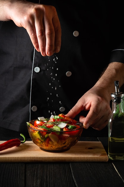 Il cuoco spruzza insalata di verdure fresche salate in un piatto su un tavolo di legno