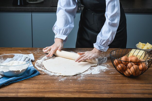 Il cuoco stende la pasta da forno sul tavolo con gli ingredienti.