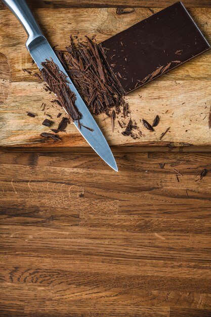 Il cuoco taglia il cioccolato con un coltello su un tavolo di legno.