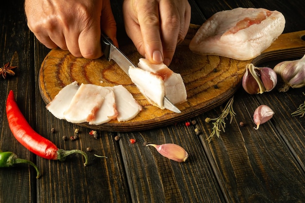 Il cuoco taglia il lardo di maiale con un coltello su una tavola da taglio in legno Il concetto di delizioso cibo contadino lardo con aglio per uno spuntino Copia spazio