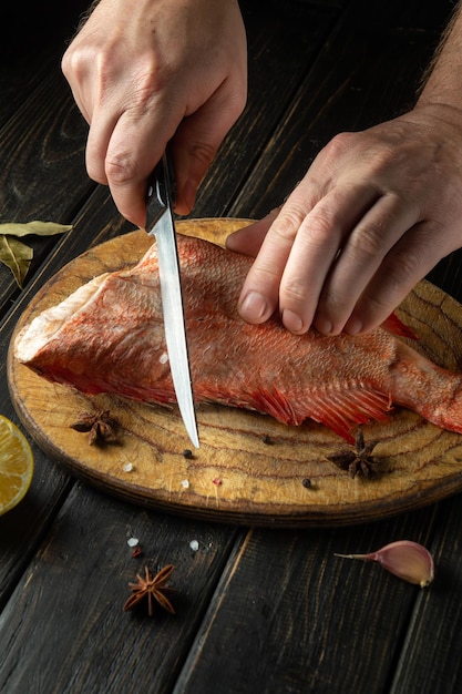 Il cuoco taglia il pesce Sebastes crudo su un tagliere da cucina