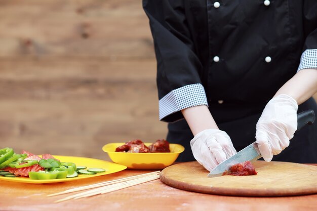 Il cuoco taglia la carne per la cottura del barbecue sul tavolo