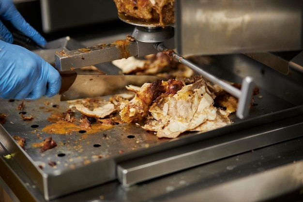 il cuoco taglia la mano dello shawarma tenendo un coltello tagliando a fette la carne da uno spiedino verticale