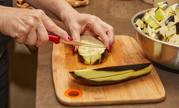 Il cuoco taglia le melanzane secondo la ricetta, su tavola di legno in cucina