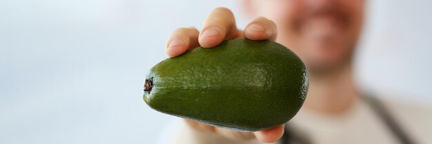 Il cuoco tiene in mano un fresco e succoso avocado verde in primo piano