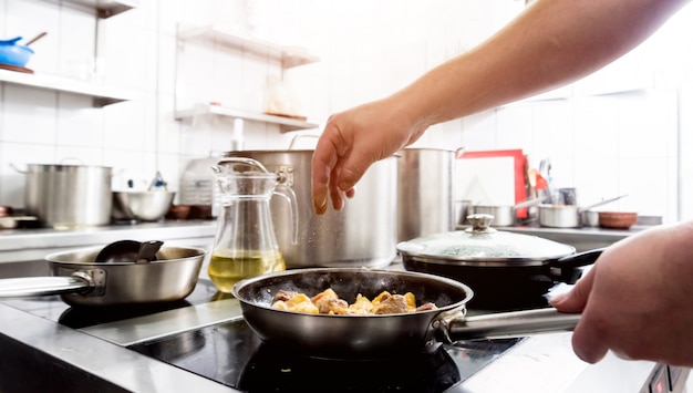 Il cuoco unico cucina le patate fritte con i pezzi di carne in una cucina del ristorante