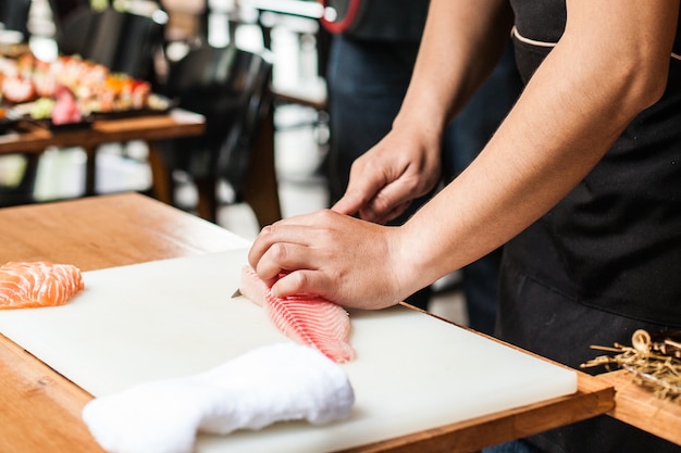 Il cuoco unico giapponese che cucina l&#39;alimento ha tagliato il pesce di color salmone sul tagliere