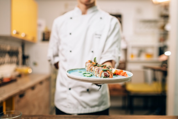 Il cuoco unico maschio tiene i rotoli di sushi sul piatto, processo di preparazione della cucina giapponese.