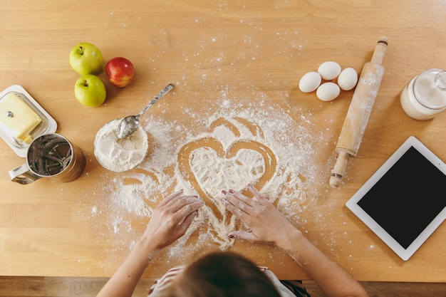 Il cuore disegnato a mano in farina sul tavolo della cucina e altri ingredienti e tablet. Vista dall'alto.