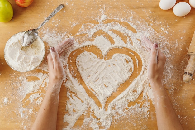 Il cuore disegnato a mano in farina sul tavolo della cucina e altri ingredienti. Vista dall'alto.