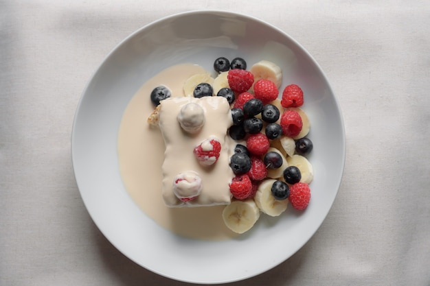 Il delizioso dessert fruttato dolce con lamponi e banana nel piatto bianco