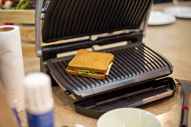 Il delizioso panino alla griglia quadrato si trova nello sfondo soft focus del primo piano della griglia elettrica aperta