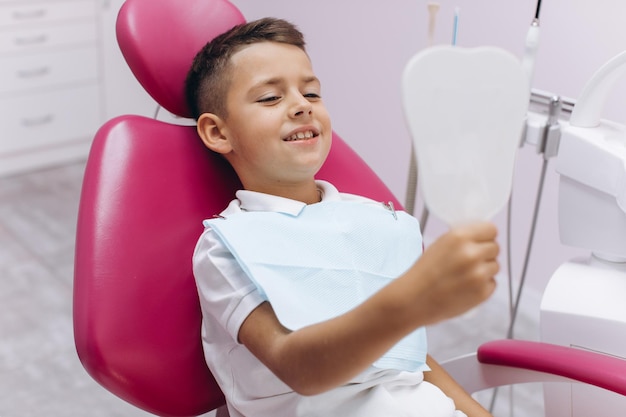 Il dentista della donna tiene uno specchio e mostra a un ragazzo sorridente il suo nuovo bel sorriso dopo una visita alla clinica dentale