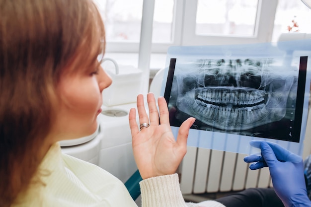 Il dentista della famiglia mostra una radiografia. una giovane donna seduta ad un ricevimento vicino a un dentista. Dentista ragazza