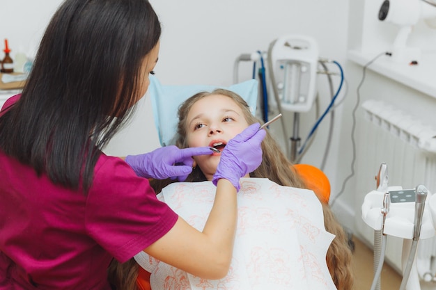 Il dentista esegue una procedura di esame su una bambina carina Bambina seduta nell'ufficio del dentista