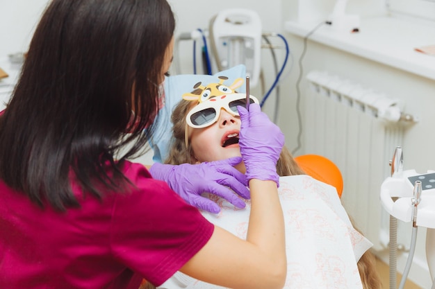 Il dentista esegue una procedura di esame su una bambina carina Bambina seduta nell'ufficio del dentista