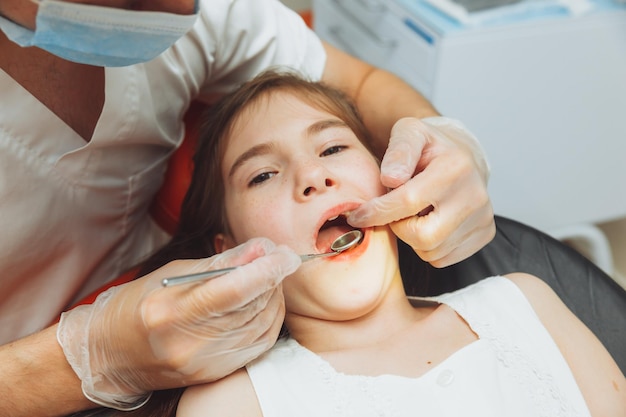 Il dentista esegue una procedura di esame su una bambina carina Bambina seduta nell'ufficio del dentista