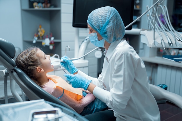 Il dentista femminile tratta i denti del paziente della bambina al concetto di odontoiatria della clinica dentale