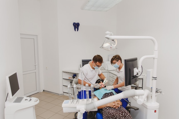 Il dentista maschio con un'assistente femmina aiuta a curare i denti di una paziente in una clinica in ufficio