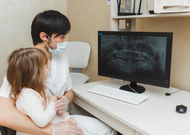 Il dentista mostra al paziente una bambina una radiografia dei denti sul computer