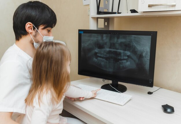 Il dentista mostra al paziente una bambina una radiografia dei denti sul computer