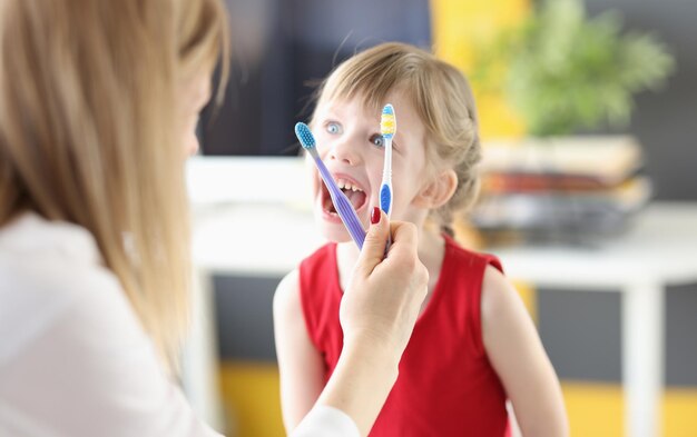 Il dentista mostra gli spazzolini da denti della bambina e i movimenti corretti per l'igiene orale