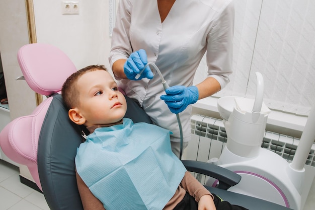 Il dentista pediatrico tratta la carie infantile e la cavità orale del ragazzo seduto sulla sedia del dentista durante il regolare controllo medico