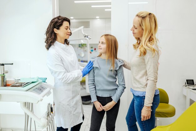 Il dentista sta parlando con una ragazza in ufficio dentistico mentre sua madre la incoraggia