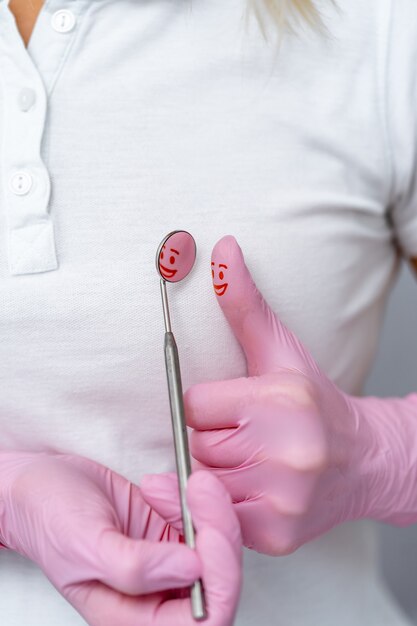 Il dentista tiene strumenti medici specifici per l'esame del paziente. Specchio dentale con riflesso del sorriso addolorato sul dito con guanti rosa. concetto di cure odontoiatriche.