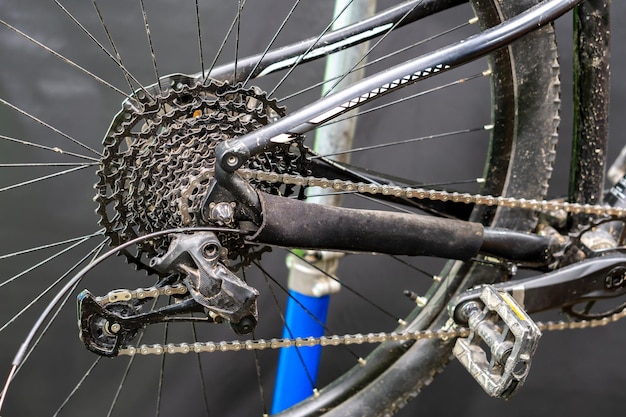 Il deragliatore posteriore di una mountain bike è un primo piano su sfondo nero Riparazione di mountain bike in officina Mountain bike sporca dopo la competizione