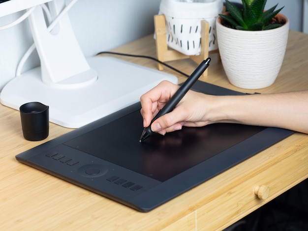 Il designer disegna su una tavoletta grafica sul posto di lavoro. Persona creativa al lavoro