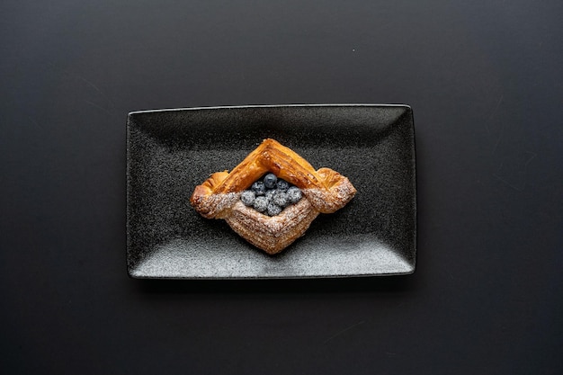 Il dessert è una piccola torta di pasta sfoglia con ripieno all'interno su un piatto da portata nero su uno sfondo nero