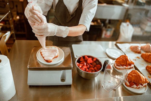 Il dipendente applica la crema dolce sul croissant dalla borsa in un negozio di panetteria artigianale