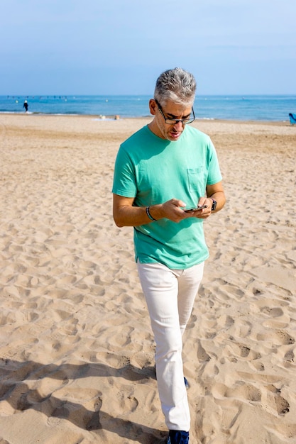 Il dirigente lascia il lavoro e cammina sulla spiaggia come metodo antistress con il cellulare in mano
