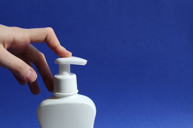 Il dito della donna preme il distributore di una bottiglia bianca di antisettico su uno sfondo blu gel antibatterico con alcool