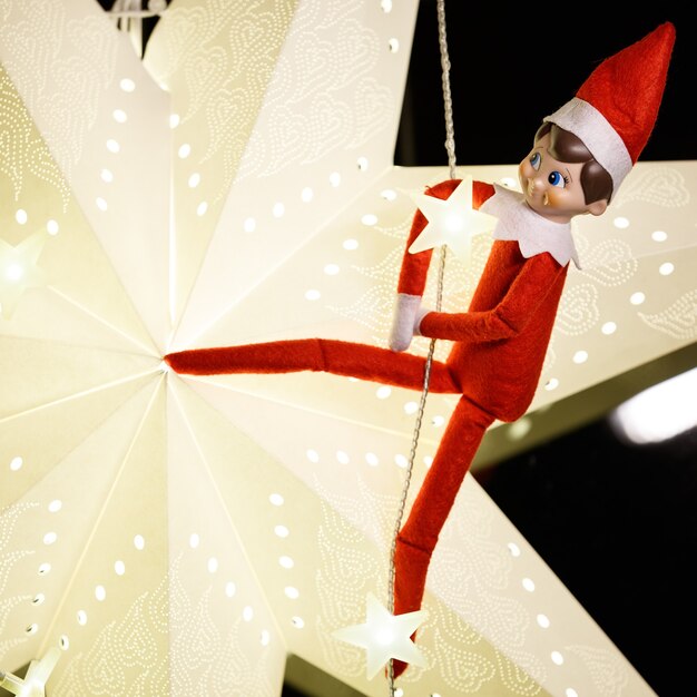 Il divertente elfo di Natale è appeso a una ghirlanda sullo sfondo di una grande stella di Natale di carta