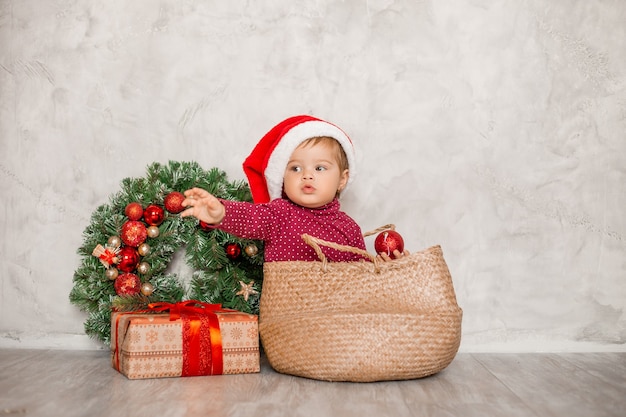 Il dolce bambino Santa si siede in un cesto di vimini con una confezione regalo