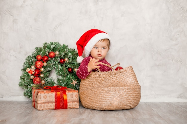 Il dolce bambino Santa si siede in un cesto di vimini con una confezione regalo