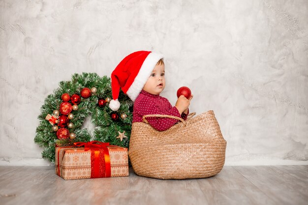 Il dolce bambino Santa si siede in un cesto di vimini con una confezione regalo