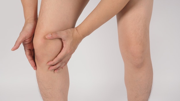 Il dolore al ginocchio maschio asiatico e le gambe ea piedi nudi è isolato su sfondo bianco.