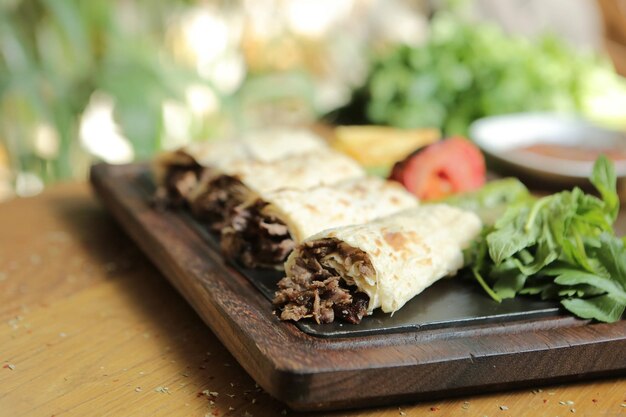 Il Doner Kebab è sdraiato sul tagliere. Shawarma con carne, cipolle, insalata giace su un vecchio legno scuro