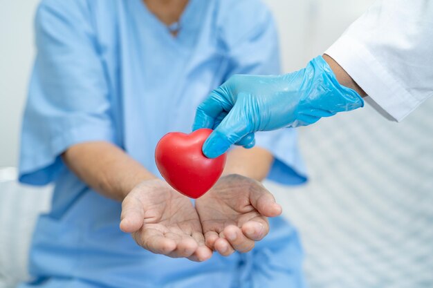 Il dottore dà il cuore rosso all'asiatica anziana o anziana signora donna paziente sana forte concetto medico