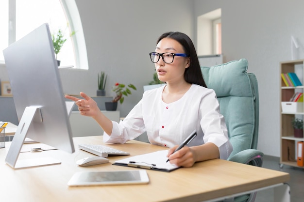 Il dottore è online, una giovane e bella dottoressa asiatica conduce una consultazione online come è