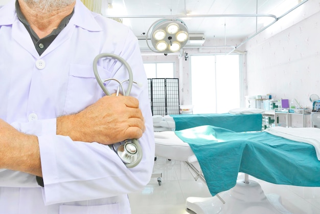 Il dottore in abito bianco tiene lo stetoscopio sullo sfondo sfocato della sala operatoria