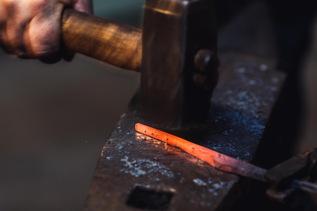 Il fabbro esegue una forgiatura artistica di metallo caldo sull'incudine.