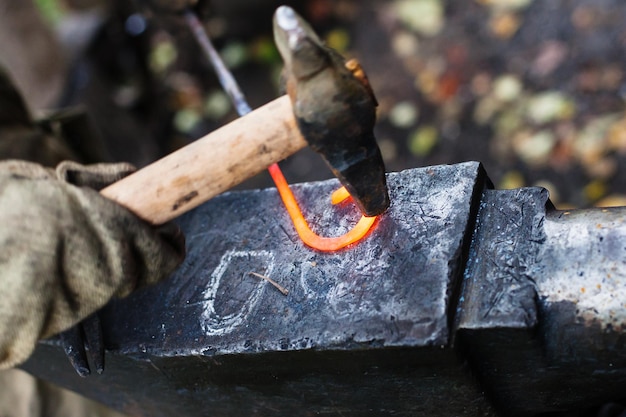 Il fabbro forgia fibbia in ferro con martello sull'incudine